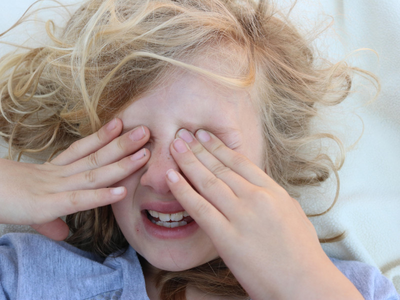 Retrato de una niña cansada con dolor con las manos frente a sus ojos.