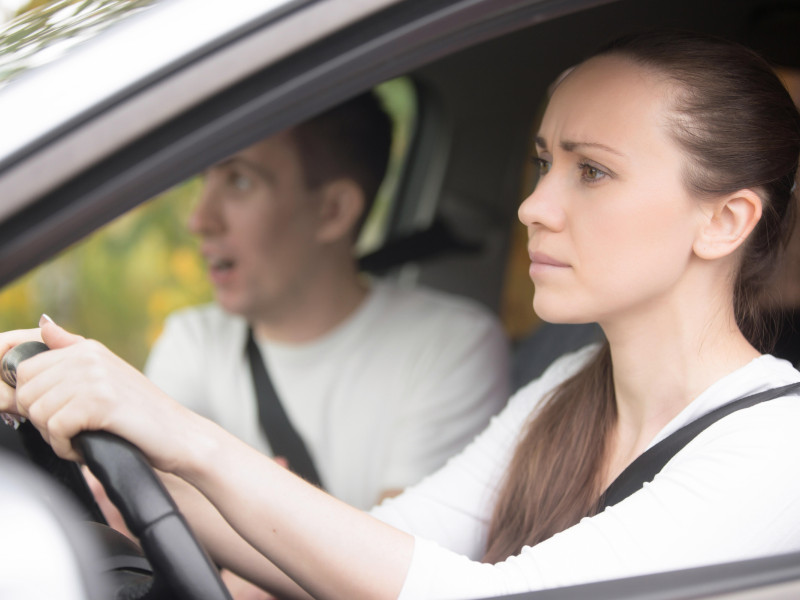 Mujer joven seria conduciendo un coche, hombre sentado a un lado