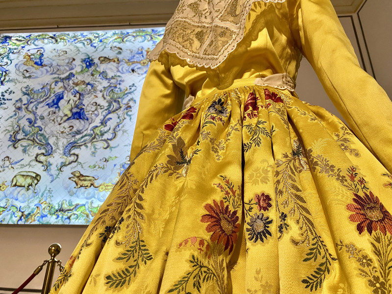 Traje de color amarillo espolinado a mano y con el dibujo valenciano San Rafael. Lo acompaña una imagen fotográfica de su propietaria, Doña María José Herrero Martí, Fallera Mayor de València en el año 1986. Cedido por Don Eduardo Puertes.