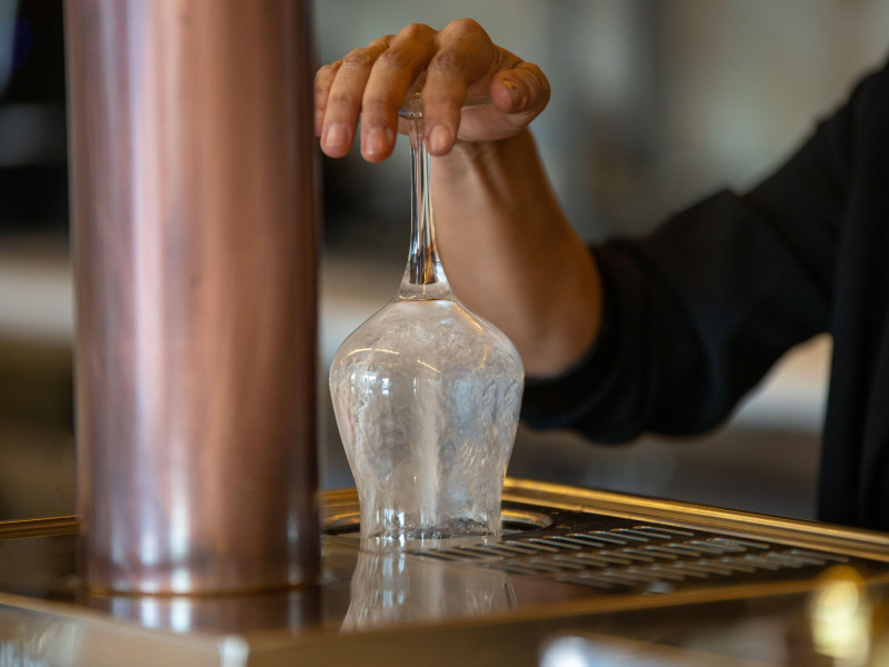 Camarero anónimo que usa un enjuagador para limpiar una copa de vino mientras trabaja en un bar moderno