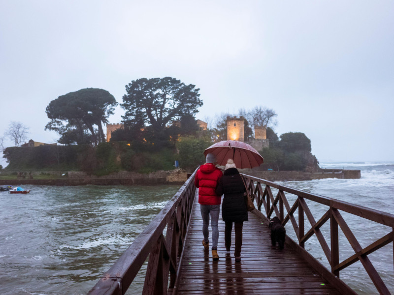 Dos personas con paraguas caminan por la pasarela en dirección a la isla de Santa Cristina, Oleiros, provincia de A Coruña.