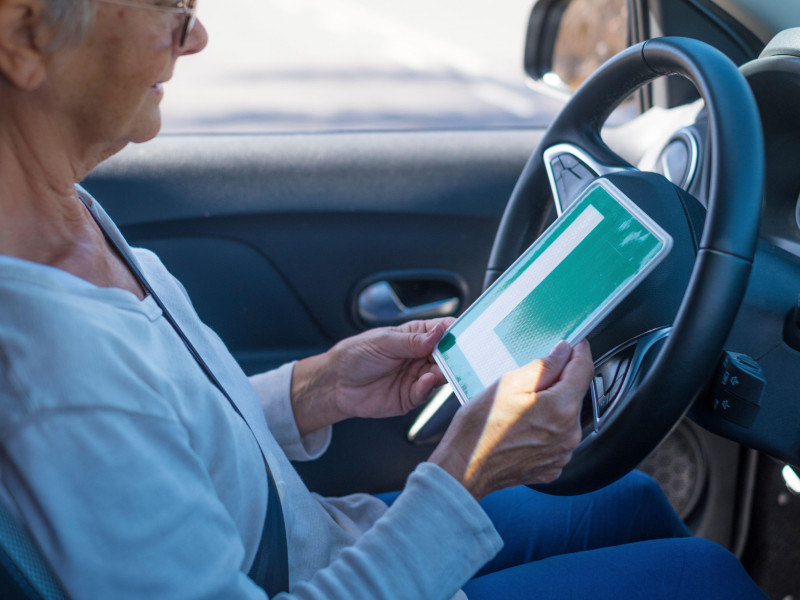 Una anciana recibe el permiso para conducir a una edad madura. Un hombre mayor mira el permiso L desde el asiento del conductor.