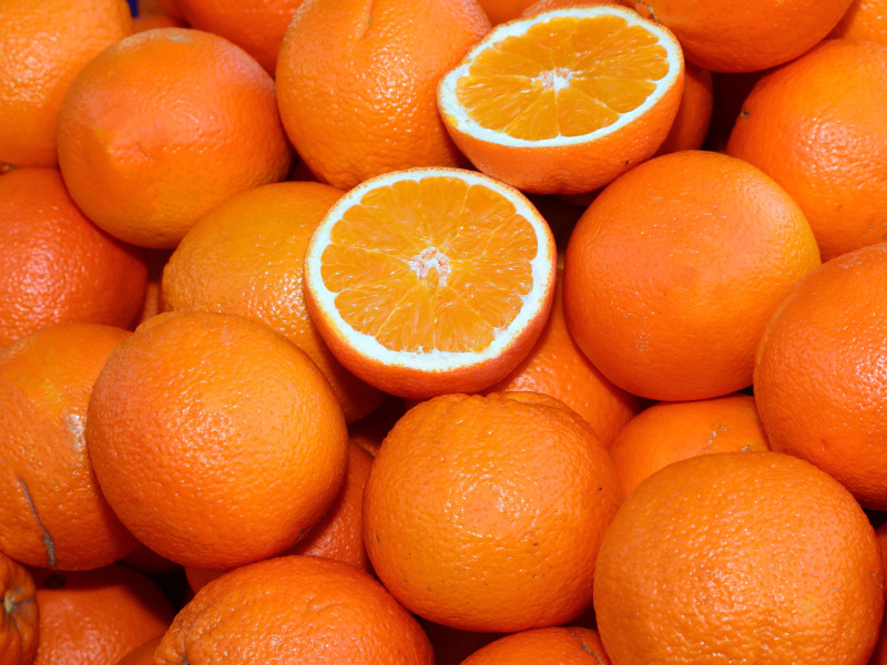 Fondo de muchas naranjas maduras y algunas cortadas por la mitad para la venta en la frutería