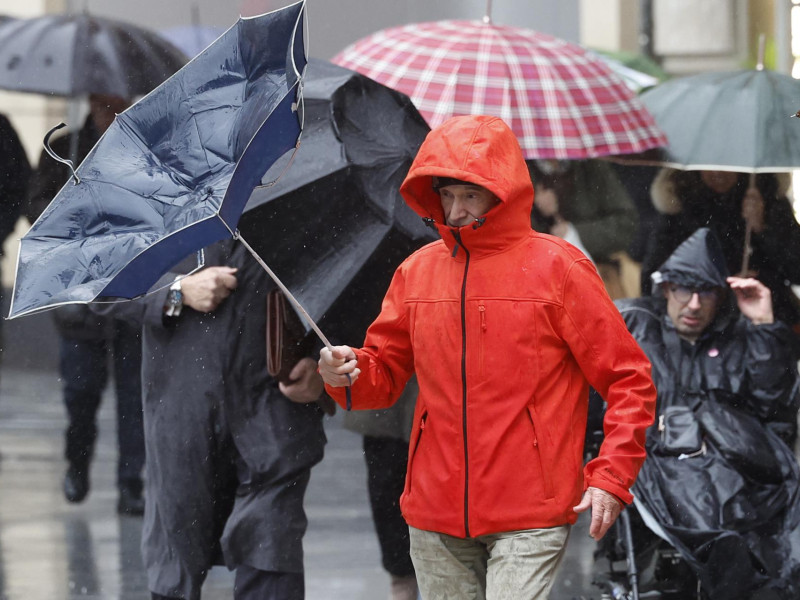 Un hombre trata de protegerse de la lluvia y el viento en Bilbao