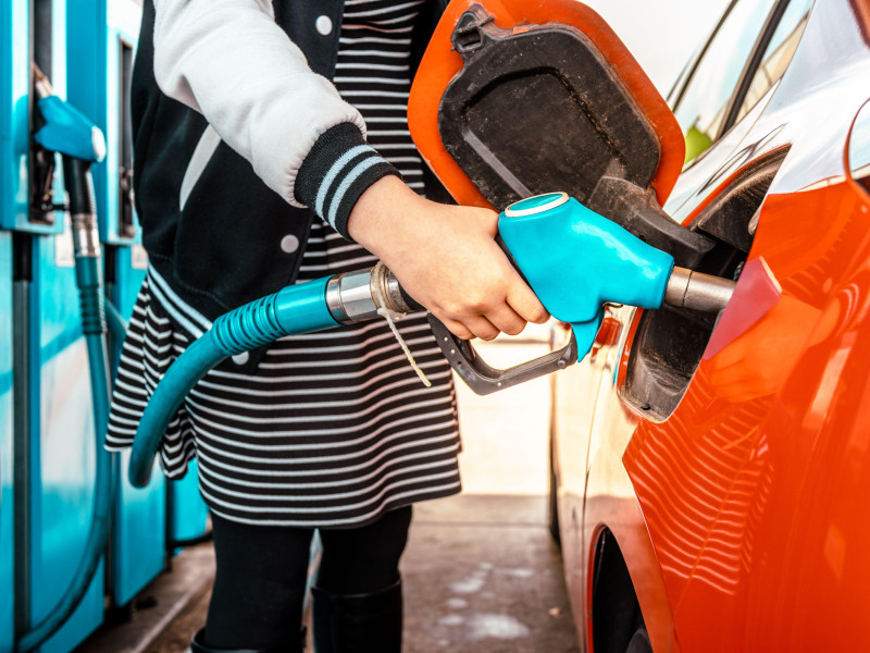 Mujer joven en una gasolinera, detalle de la mano repostando un coche