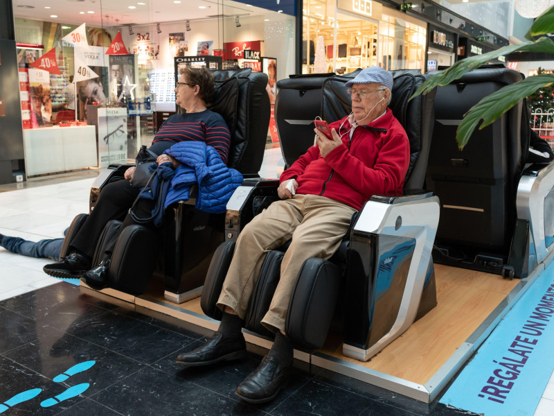 Pareja mayor sentada en una silla de masajes en el centro comercial As Cancelas, Santiago de Compostela