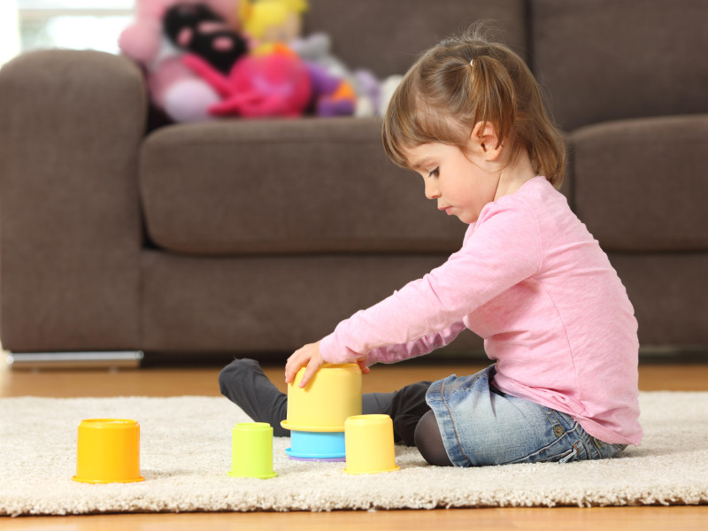 Vista lateral de un niño jugando con juguetes sentado en el suelo de la sala de estar en casa.