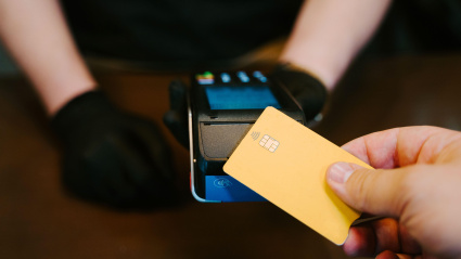 Persona irreconocible sosteniendo una tarjeta de crédito y pagando en un punto de venta.