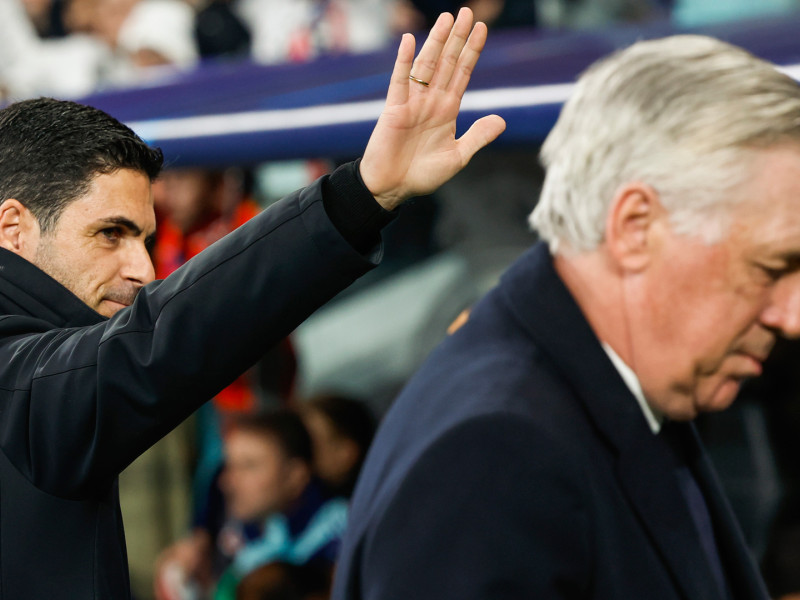 Carlo Ancelotti con gesto serio; al fondo, Mikel Arteta saluda desde el banquillo