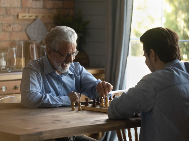Un padre anciano entusiasta juega una partida amistosa de ajedrez con su hijo adulto