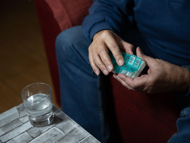 Primer plano de las manos de un señor mayor tomando pastillas de su pastillero.