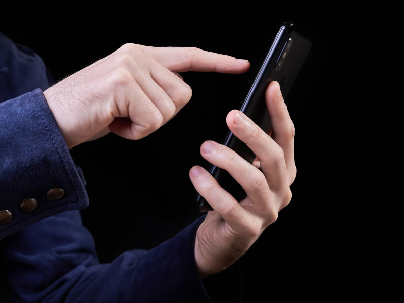 Un hombre presiona su dedo sobre la pantalla de un teléfono inteligente sobre un fondo oscuro.