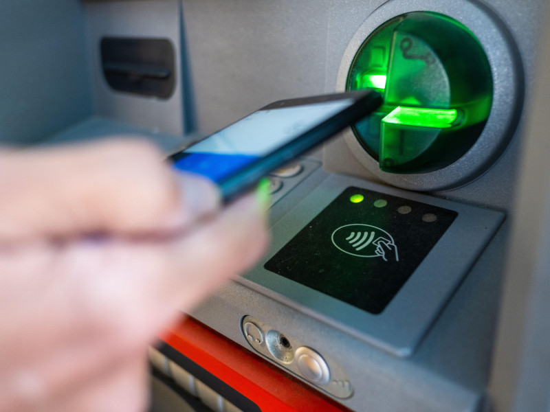Una persona opera con su teléfono inteligente en un cajero automático utilizando la opción inalámbrica o sin contacto
