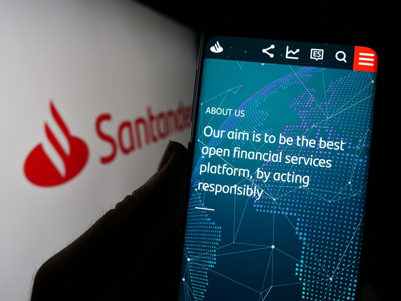 Persona sosteniendo un teléfono móvil con la página web del banco español Banco Santander SA en la pantalla frente al logotipo