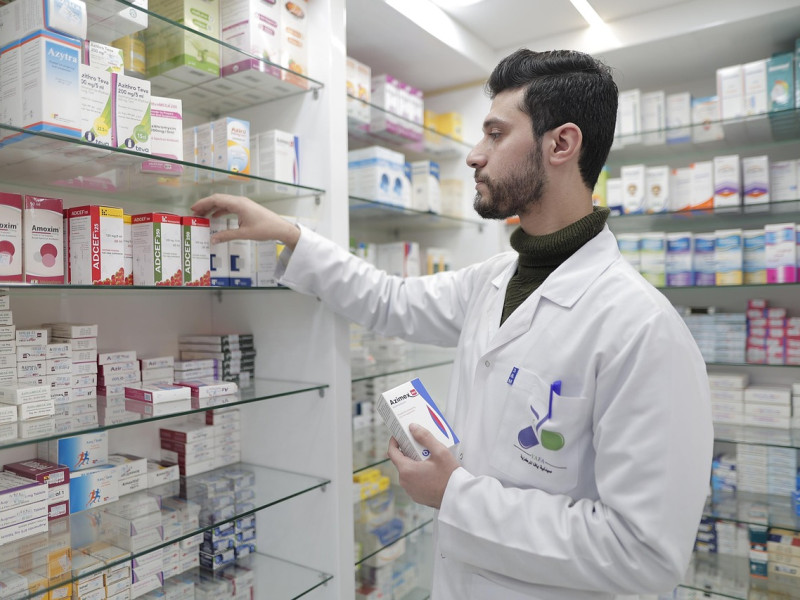 Un farmacéutico busca un medicamento en la estantería.