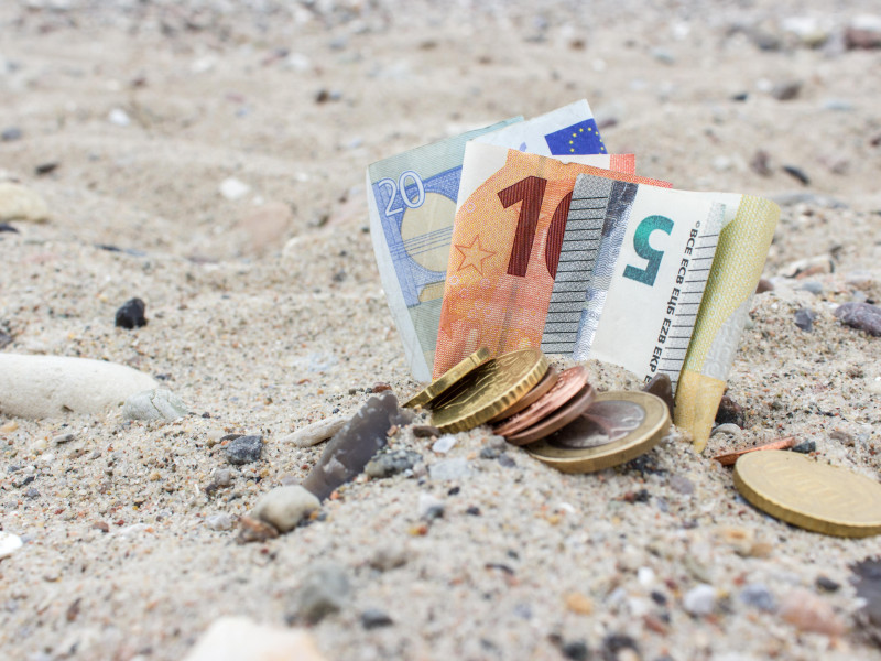 Monedas, billetes, piedras y conchas en la arena