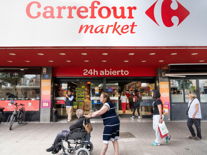 La gente pasa junto a la cadena multinacional francesa de supermercados Carrefour y su tienda de barrio abierta las 24 horas, Carrefour Market, en España.