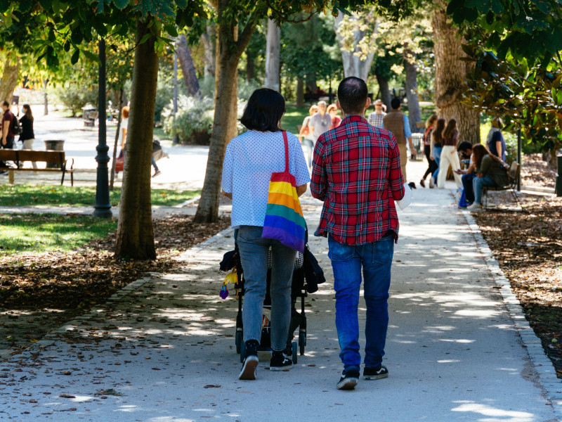 Pareja joven paseando con un cochecito de bebé en el parque del retiro de Madrid.
