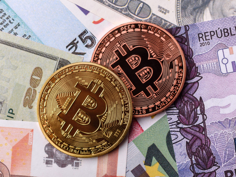 Bitcoin metálico redondo sobre un fondo de billetes de papel de diferentes monedas