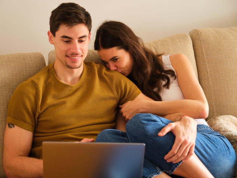 Una pareja española ve una película en el ordenador mientras se abrazan y se besan.