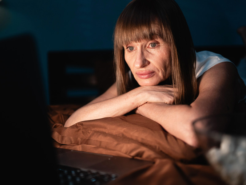 Mujer acostada en la cama viendo una película en la computadora en un dormitorio oscuro por la noche