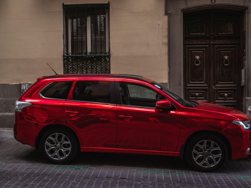 Un lujoso y caro SUV rojo brillante está estacionado en una calle de una ciudad antigua.
