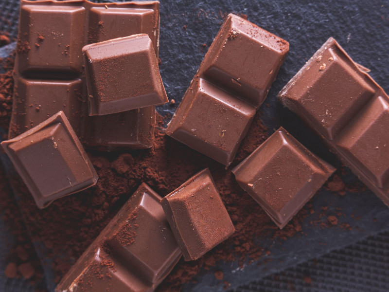 onzas de chocolate partido sobre cacao en polvo y fondo de pizarra negra