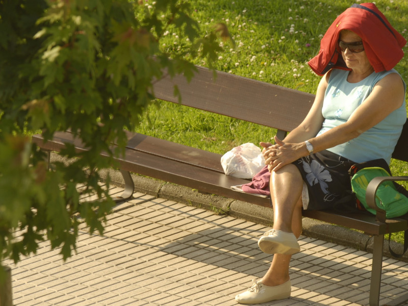 Una mujer se protege del calor, sentada en un banco, en Asturias