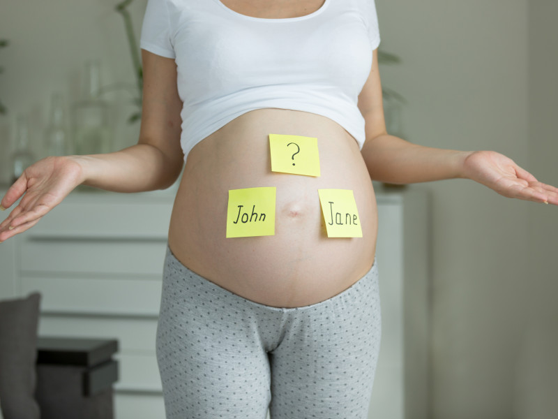 Concept of choosing baby's name. Pregnant woman with names on belly