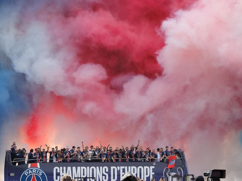 El equipo y el personal del PSG celebran bajo el humo coloreado con los colores nacionales franceses durante un desfile de la victoria del equipo en un autobús descapotable en el bulevar de los Campos Elíseos en París, Francia.
