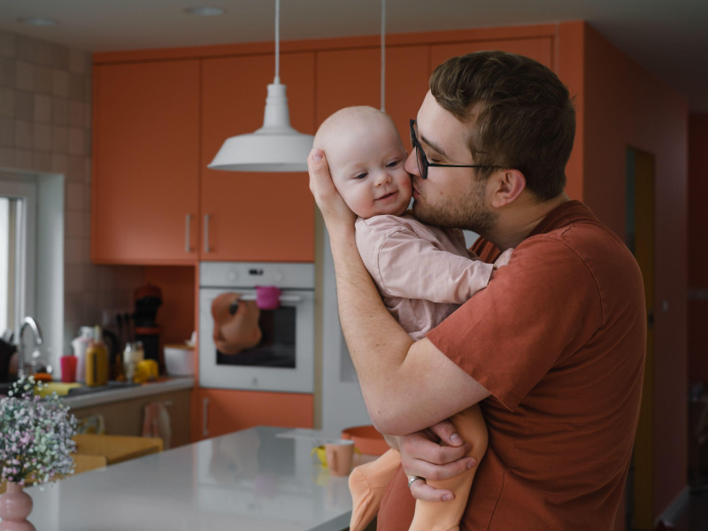 Papá con su pequeña niña en sus manos acurrucándose en la cocina de casa, cuidando a la bebé.