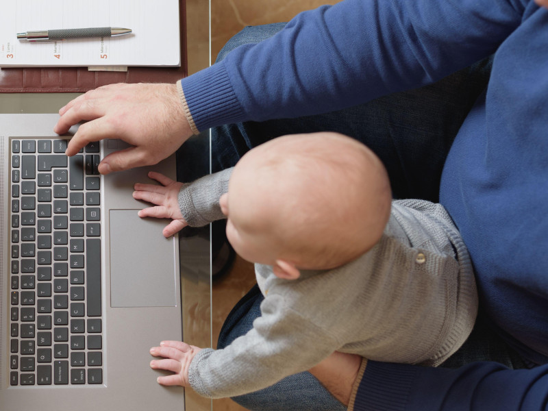 Joven administrativo teletrabajando y cuidando a su bebé de 6 meses