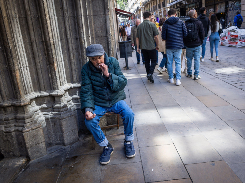 Un anciano sentado afuera de una iglesia en Barcelona, España, pidiendo limosna de dinero.