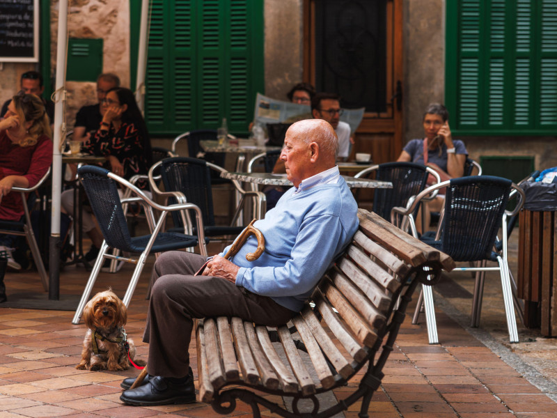 Un anciano con su perro descansa en un banco en un típico pueblo de montaña cerca de un café