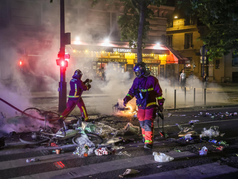 Los bomberos franceses extinguen un incendio callejero mientras estallan enfrentamientos entre la policía francesa y los aficionados del PSG que celebran la victoria de su equipo en la final de la UEFA Champions League entre el Paris Saint-Germain y el Internazionale Milano, París, Francia.