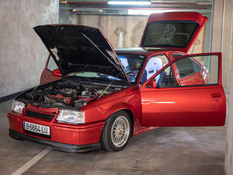 Opel Kadett E clásico en rojo con las puertas y el capó abiertos en un garaje