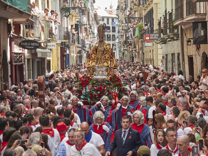 Decenas de personas participan en la procesión en honor a San Fermín, patrón de Pamplona, a 7 de julio de 2023, en Pamplona, Navarra (España). Miles de pamploneses ataviados de blanco y rojo han salido a las calles de Pamplona hoy, día grande de las fiestas de San Fermín, para arropar al santo en su recorrido por el Casco Antiguo de la ciudad. La figura de San Fermín ha estado arropada por la Comparsa de Gigantes y cabezudos, las cruces parroquiales, la Cruz Arzobispal, los gremios y cofradías, dantzaris municipales, txistularis, clarinero y timbales, el cabildo Catedralicio Arzobispo de Pamplona, la bandera de la ciudad, maceros, libreas, la Corporación municipal, Policía Municipal, escolta de gala y La Pamplonesa. Las fiestas en honor a San Fermín, comenzaron ayer, 6 de julio con el tradicional chupinazo y se prolongan hasta el 14 de julio con el cántico del ‘Pobre de mí’. Un año más, la calle es el escenario principal de las fiestas de San Fermín, fechas en las que se han programado 542 actos oficiales, 300 de ellos de carácter musical. Esta fiesta que atrae a millones de visitantes cada año por su ambiente festivo y sus populares encierros, está declarada de Interés Turístico Internacional.