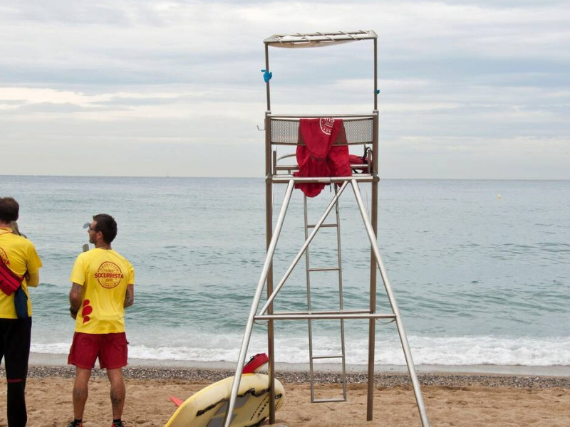 2SYR9KJ 2SYR9KJ Two young lifeguards on the beach next to a lifeguard's chair on a cloudy day, San Sebastian beach, Barceloneta beach, Barcelona, Spain