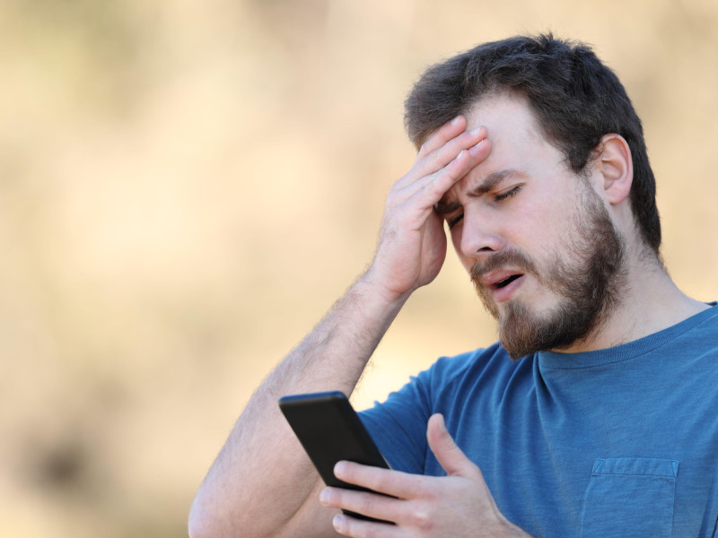 Un joven preocupado mientras mira la pantalla de su teléfono móvil