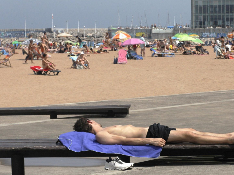 Un joven toma el sol en el paseo de la playa de Poniente, en Gijón