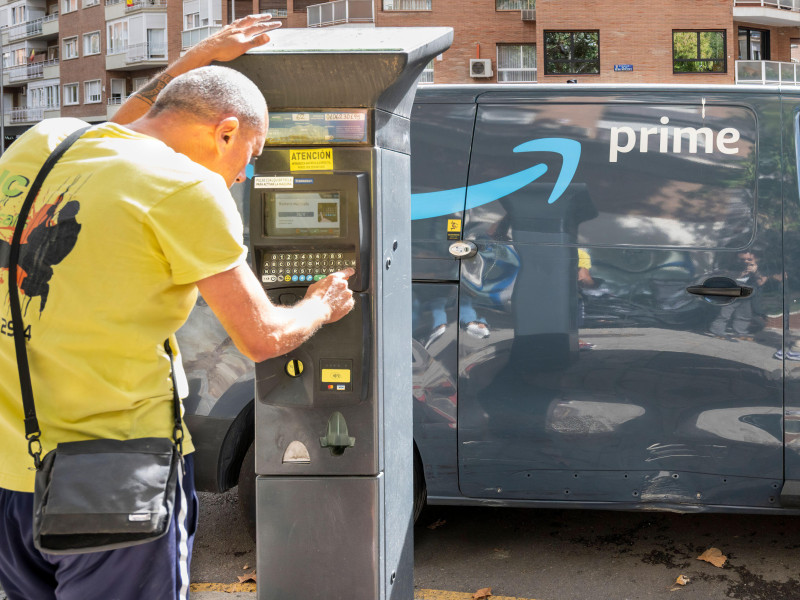 Un hombre se las arregla con un parquímetro mientras una furgoneta del servicio estadounidense de suscripción de reparto de pago propiedad de Amazon