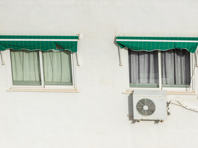 Dos ventanas cerradas con persianas y sistema de aire acondicionado instalado en un caluroso día de verano en España.
