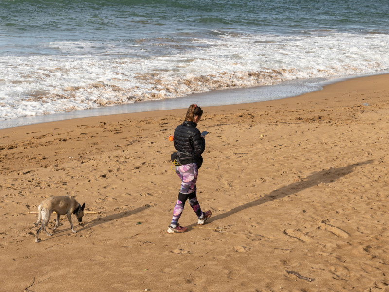 Una mujer pasea a un perro mientras escribe mensajes de texto en su móvil en la Playa de Zarautz en Zarautz