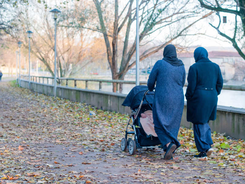 Dos mujeres musulmanas con un bebé caminando por una calle peatonal junto al río, Manlleu, Cataluña