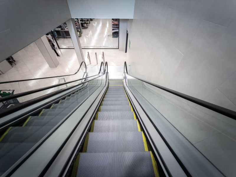 Vista hacia abajo desde lo alto de una escalera mecánica mientras desciende hacia la planta de comestibles de un supermercado de Barcelona.