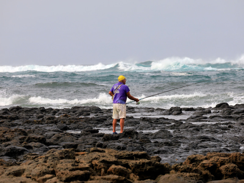 Hombre solitario pescando con caña en la costa volcánica rocosa de Fuerteventura, Islas Canarias