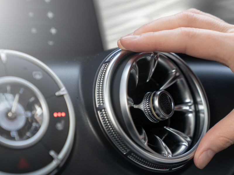 Una mano ajusta suavemente una elegante y estilizada salida de aire del automóvil para garantizar una comodidad óptima y un control climático eficaz.