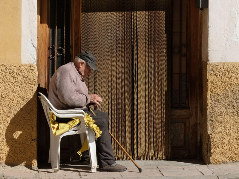 Un anciano con gorra de camionero se sienta al sol afuera de su casa en Libros, cerca de Teruel.