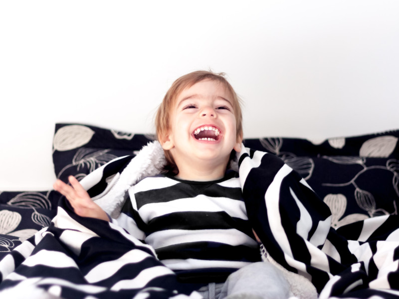Niño sentado en una cama envuelto en una manta riendo