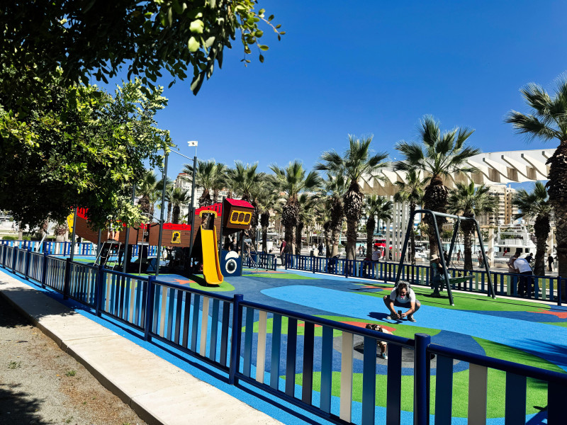 Parque infantil en Málaga rodeado de palmeras y coloridos equipamientos.